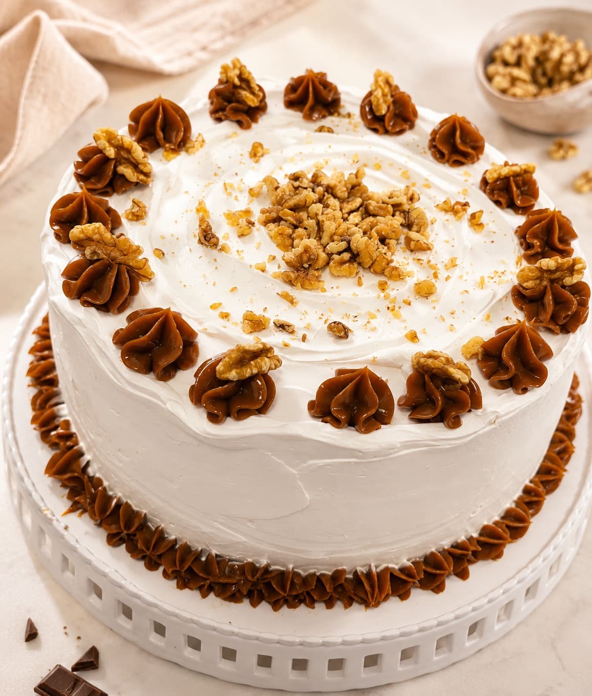 Torta cubierta de crema blanca, con nueces enteras y rosetones de manjar en el borde